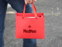 A photo of a MedMen customer carrying a red MedMen shopping bag.