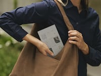 A woman wearing a blue shirt putting her reMarkable Paper Pro Move tablet into her brown shoulder bag.