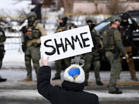 An onlooker holds a sign that reads "Shame" as members of law enforcement work the scene following a suspected shooting by an ICE agent during federal law enforcement operations on January 07, 2026 in Minneapolis, Minnesota. According to federal officials, the agent, “fearing for his life” killed a woman during a confrontation in south Minneapolis.