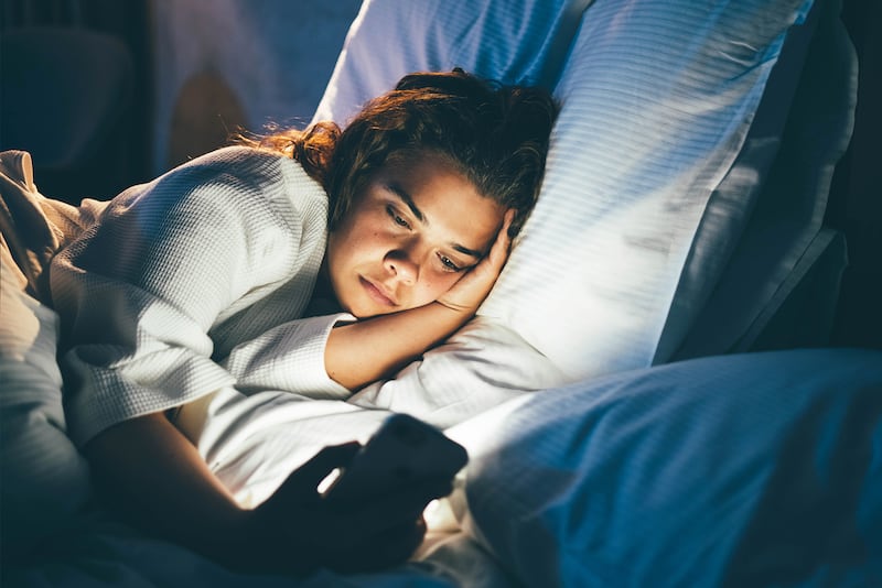 Young woman laying in bed and using her phone.