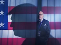 Michael Wolff Stands in front of an American Flag with a distinctive silhouette shadowed across him.