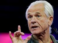 Peter Navarro speaks on stage at an event with his right hand raised.