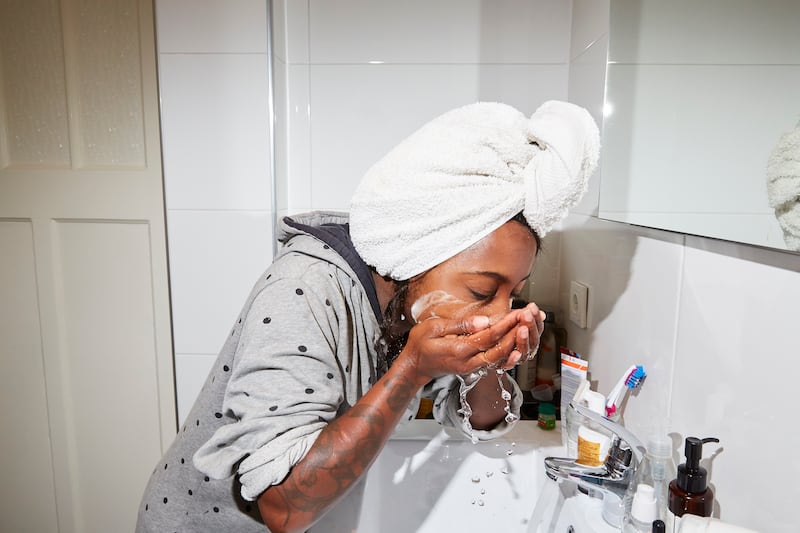 A young woman washes her face in her bathroom
