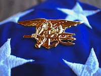 Navy SEAL trident rests atop a folded American flag in remembrance of the brotherhood
