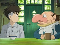 A still from ‘The Boy and the Heron,’ featuring a boy and a man in an animal outfit sitting at a table.