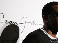 Sean Combs smiles in front of a logo for his fashion brand, Sean John.