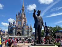 The entrance to Magic Kingdom at Walt Disney World, showing a statute of Walt Disney in the foreground and a castle in the background.