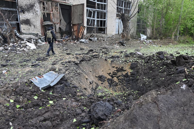 A law enforcement officer walks by a crater in Ukraine.