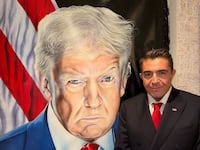 Paolo Zampolli posing in front of a portrait of Donald Trump.