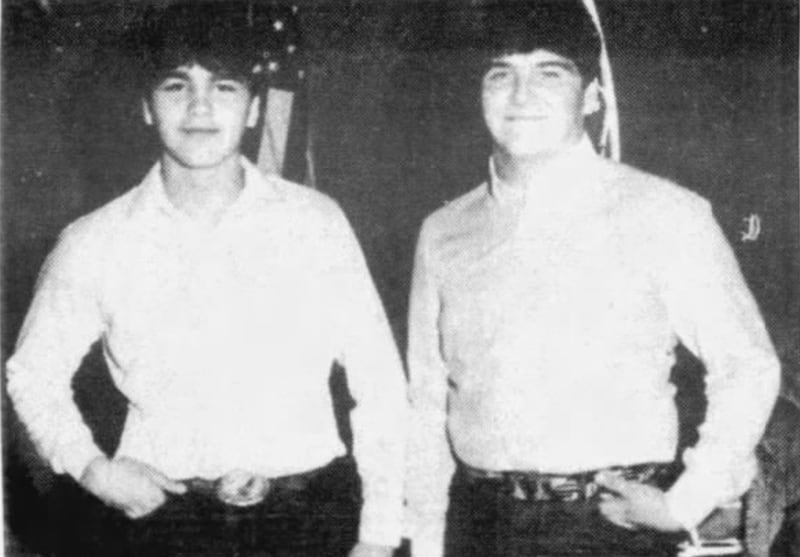 Two teenagers in black and white. Both are wearing white shirts, jeans and one has a Texas belt buckle. They are smiling.