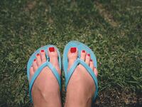 Red toenail polish and blue plastic flip-flops on green grass.