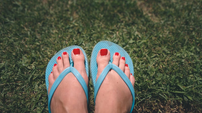 Red toenail polish and blue plastic flip-flops on green grass.
