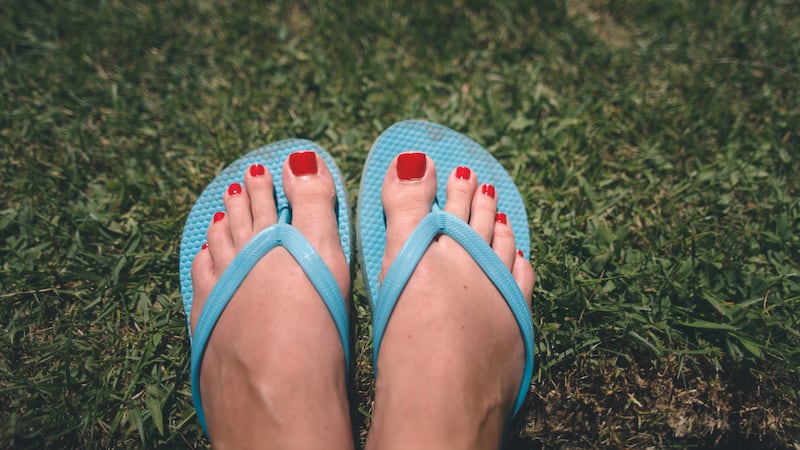 Red toenail polish and blue plastic flip-flops on green grass.
