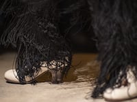 A photo of a flamenco dancer’s feet, in white shoes. The bottom of a black flamenco-style dress can be seen.
