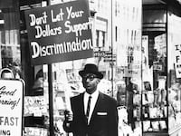 A photo including a Picketer demanding an end to lunch counter segregation made their first appearance outside a Woolworth store in Lynchburg, Virginia.