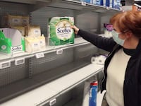 A woman wearing a protective face mask looks for toilet paper in a supermarket.