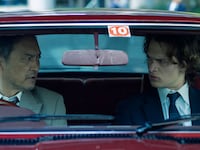Ken Watanabe and Ansel Elgort inside of a car looking at each other in a still from ‘Tokyo Vice’