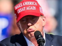 Donald Trump purses his lips while raising his hand on stage at a campaign rally.