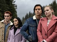 Four teenagers in coats stand together outside, looking mournful.