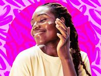 A photo illustration of a young African American woman smiling while applying a beauty cream on her face on a purple and pink background.