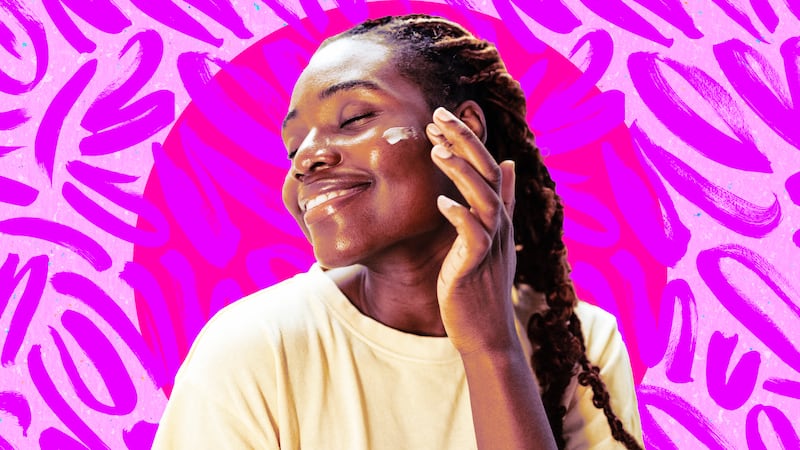 A photo illustration of a young African American woman smiling while applying a beauty cream on her face on a purple and pink background.