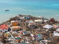 A drone-eye view of shattered houses on a peninsula, behind it is crystal-clear water