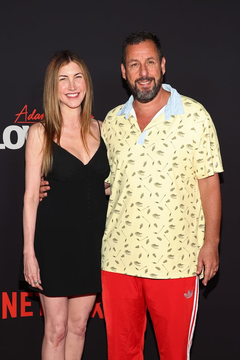Jackie Sandler poses beside husband Adam Sandler as he wears a short-sleeved shirt and track suit pants, while attending Netflix’s “Adam Sandler: Love You” in 2024.