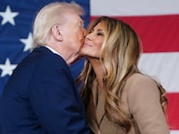 President Donald Trump kisses the First Lady Melania Trump on the cheek in from of a giant USA flag