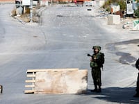 A photograph of Israeli soldiers standing guard on a blocked road, as the entrance to Hebron is closed, in the Israeli-occupied West Bank, October 8, 2023.