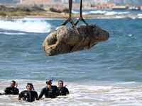 TOPSHOT - Divers watch as a crane pulls an artifact from the waters at Abu Qir bay in Alexandria on August 21, 2025, as part of an event organized by the Ministry of Tourism and Antiquities to recover sunken antiquities.