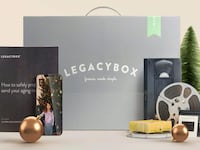 Legacybox kit with VHS tapes, film reels, photos, and smartphone showing digitized family memories