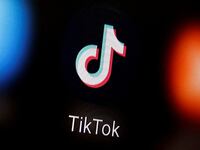 A TikTok logo is illuminated on a black screen with blurred apps on either side of it.