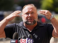 Alex Jones raises his hands while speaking at a press conference.