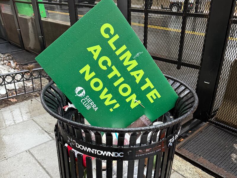 A sign saying Climate Action Now in a trash can