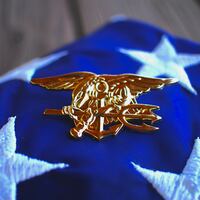 Navy SEAL trident rests atop a folded American flag in remembrance of the brotherhood