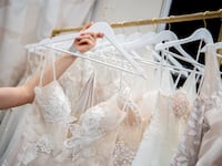 A woman takes a wedding dress off a rack with several dresses.