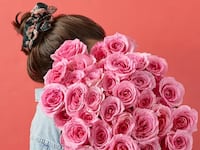 Farm-fresh pink rose bouquet from Bouqs held against a coral background, perfect for Valentine’s Day gifting
