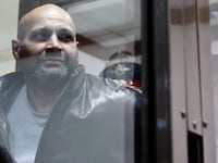 "One of the defendants in the murder trial of Russian journalist and human rights activist Anna Politkovskaya, Sergei Khadzhikurbanov is escorted into a glass-walled cage before a court hearing in Moscow,