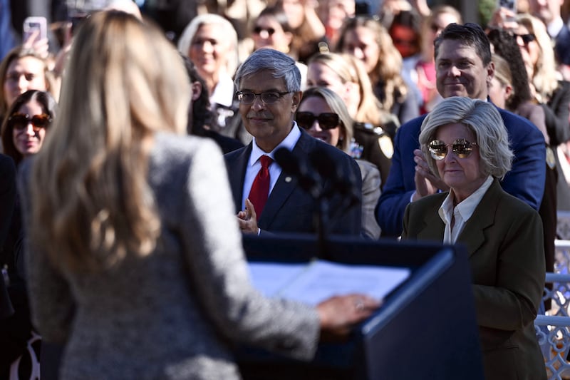 National Institutes of Health director Jayanta Bhattacharya (C) and White House Chief of Staff Susie Wiles react as US First Lady Melania Trump speaks during an executive order ceremony in the Rose Garden of the White House in Washington, DC, on October 19, 2026. The executive order aims to a create a Women's Health Division at the National Institutes of Health (NIH) and a White House Women's Health Task Force.