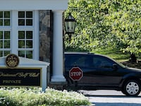 A black car pulls out from behind a sign that says Trump National Golf Club.