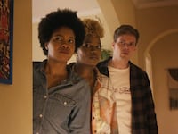 Three people peer from behind a wall.