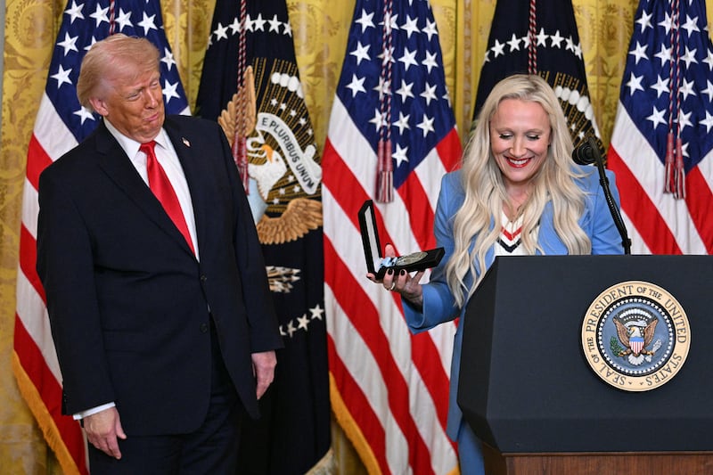 President Donald Trump reacts as U.S. bobsledder Kaillie Humphries announces she is awarding him with an Order of the Ikkos during a Women's History Month event in the East Room of the White House in Washington, DC, on March 12, 2026. Medal-winning team USA athletes can award an Ikkos award to recognize people who have been supportive in their journey to the Games.