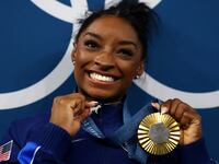 Simone Biles holds a goat necklace and her gold medal while smiling
