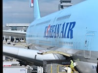 A photo of a Korean Air jetliner parked at the gate, as viewed from a window inside the terminal.