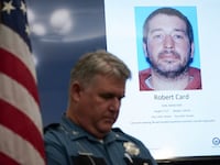 A police officer stands next to a screen displaying the picture of the suspected shooter, during a press conference following the deadly mass shooting, at City Hall in Lewiston, Maine.