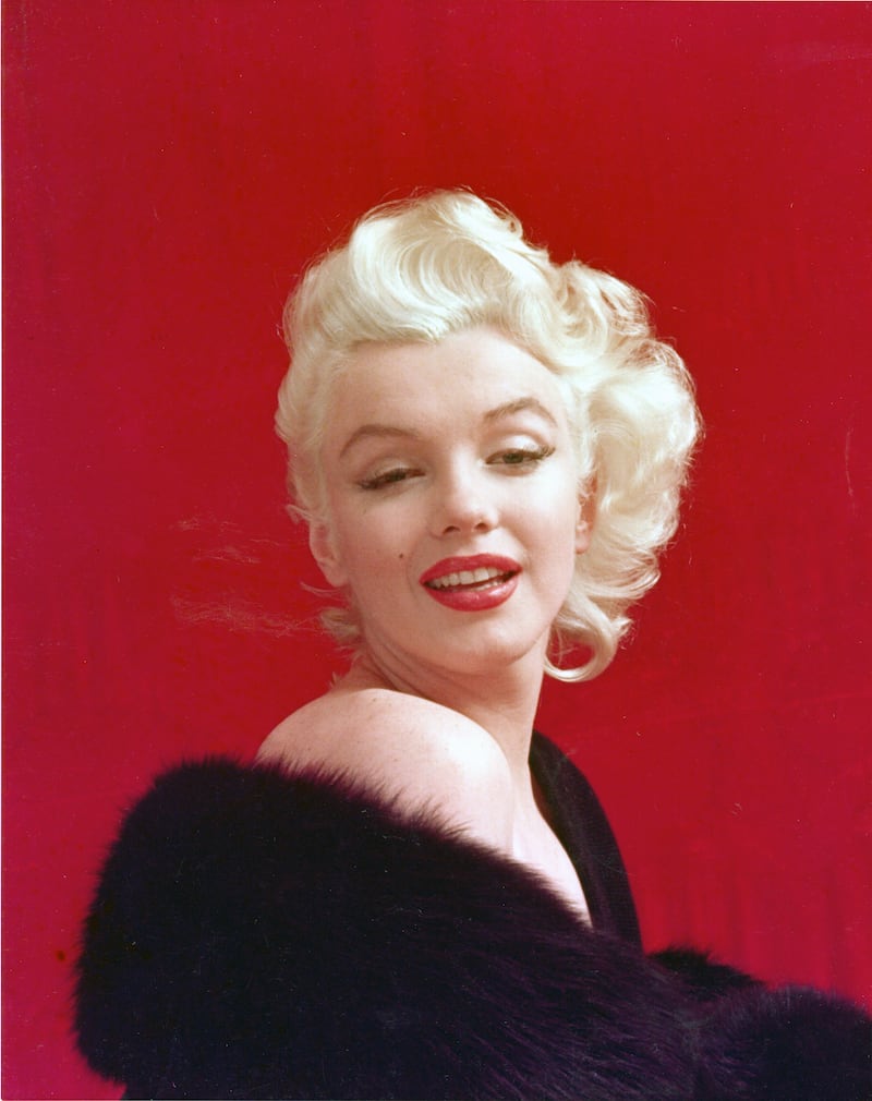 a portrait of Marilyn Monroe with a black fur coat, red lipstick, and curls in her blond hair