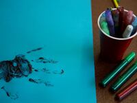 A handprint in glitter glue next to a cup of glitter pens