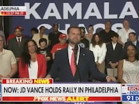 J.D. Vance delivers a speech in front of a crowd and a poster that reads “KAMALA.”