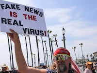 A protester holds a placard that says Fake News Is The Real Virus during the demonstration. Citizens staged a protest in front of the Huntington Beach Pier to demand for the reopening of the California economy.
