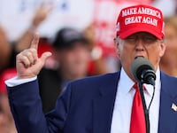 Donald Trump raises his hand while speaking on stage.